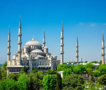 The Blue Mosque in Istanbul, Turkey, showcases its stunning architecture on a sunny day, surrounded by vibrant greenery