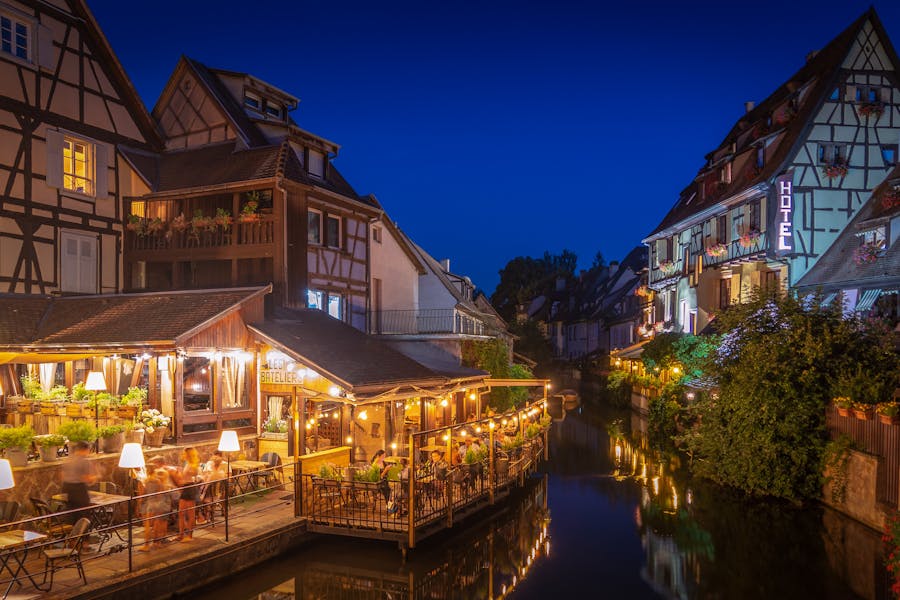 Colmar Little Venice canal at twilight with half-timbered houses, riverside restaurants and warm lights.