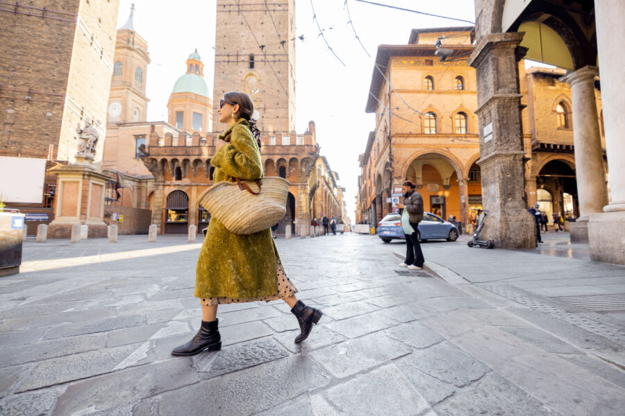 Stylish  tourist walks the streets of Bologna, famous towers behind her, embodying the essence of Italian street fashion