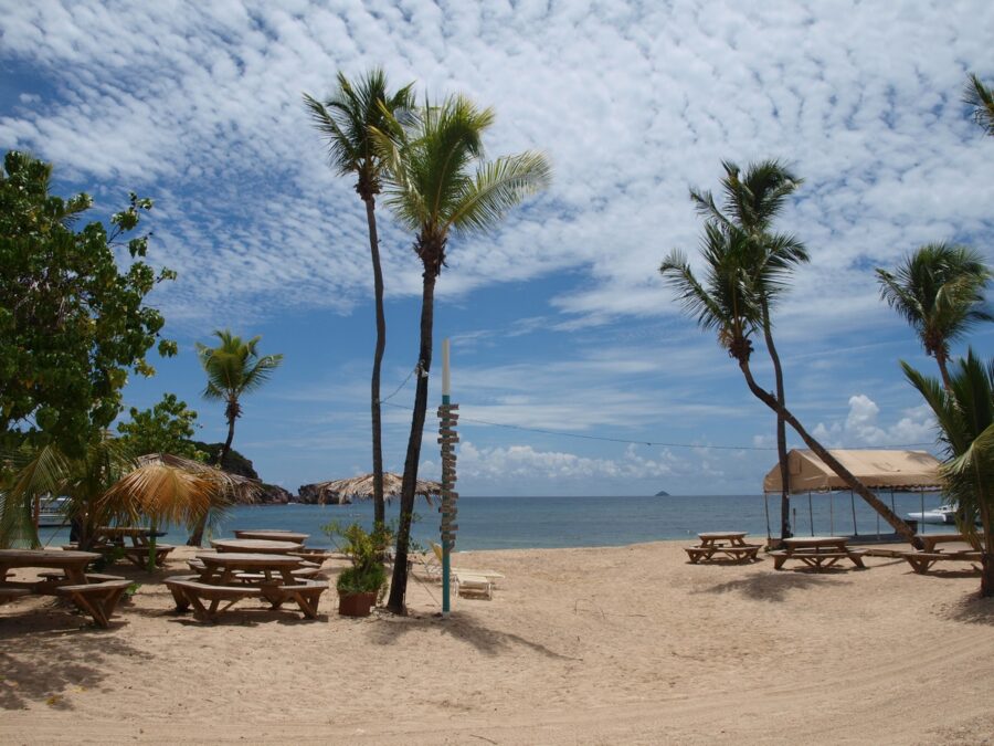 Sandy beach at Bolongo Bay, St. Thomas, featuring picnic tables and colorful umbrellas for shade.