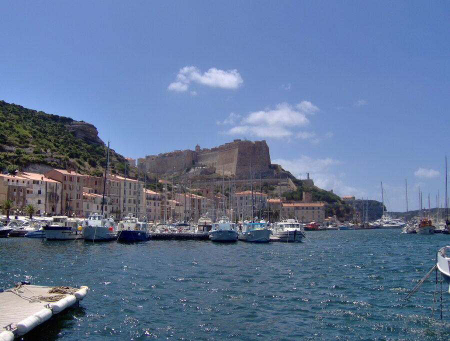 Bright blue sky dotted with white clouds above the scenic Port de Plaisance and Citadelle in Bonifacio, Corsica.