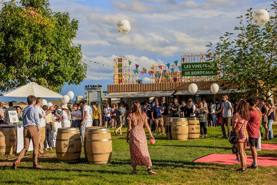 Vibrant Bordeaux wine festival with attendees enjoying wine, sunny day, and lush green setting.