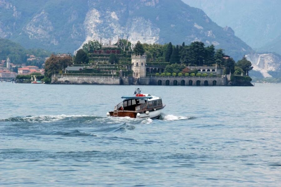 Boat gliding on water beside a castle, showcasing the Borromean Islands Private Boat Taxi experience.