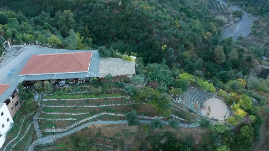 Aerial view of the Botanical Garden of Crete, showcasing a large building nestled on a hillside surrounded by greenery.