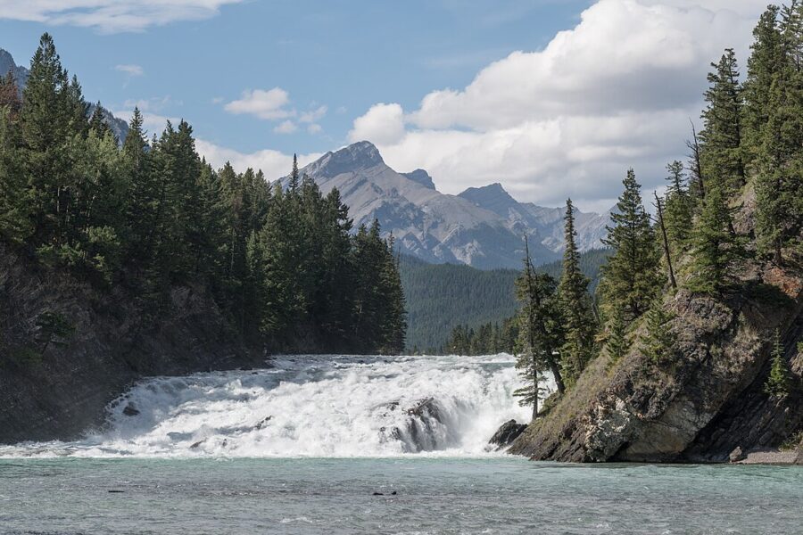 Bow Falls in Canada, showcasing a waterfall cascading into a river, framed by vibrant green trees in the background.
