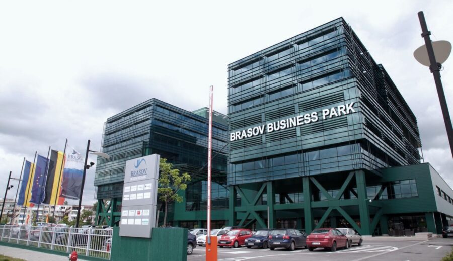 Green building featuring a sign that says "Brasov Business Park ," located in Brasov, with a sunny sky in the background.