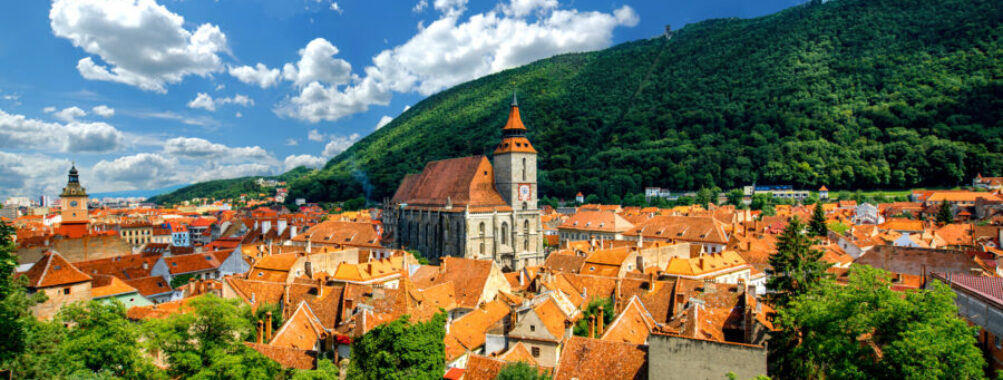 Panoramic view of Brașov cityscape in Romania, showcasing historic buildings and the surrounding Carpathian Mountains.