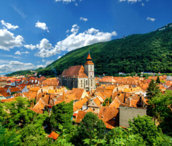 Panoramic view of Brașov cityscape in Romania, showcasing historic buildings and the surrounding Carpathian Mountains.