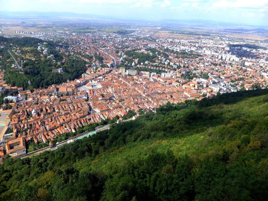 Aerial view of Brasov, Romania, showcasing the cityscape from the top of a hill with surrounding mountains.