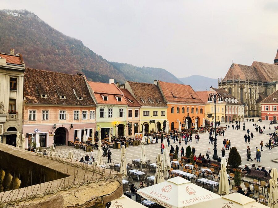 Vibrant scene in Brașov, Romania, featuring a town square with numerous people and various buildings.