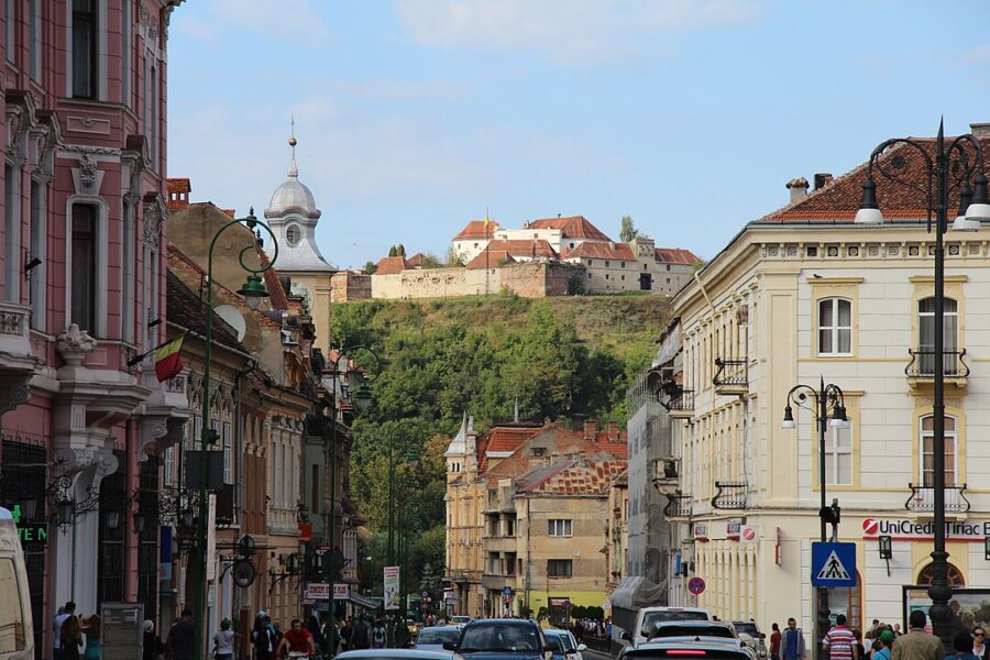 City street in Brașov, Romania, lined with cars and showcasing a majestic castle in the background.