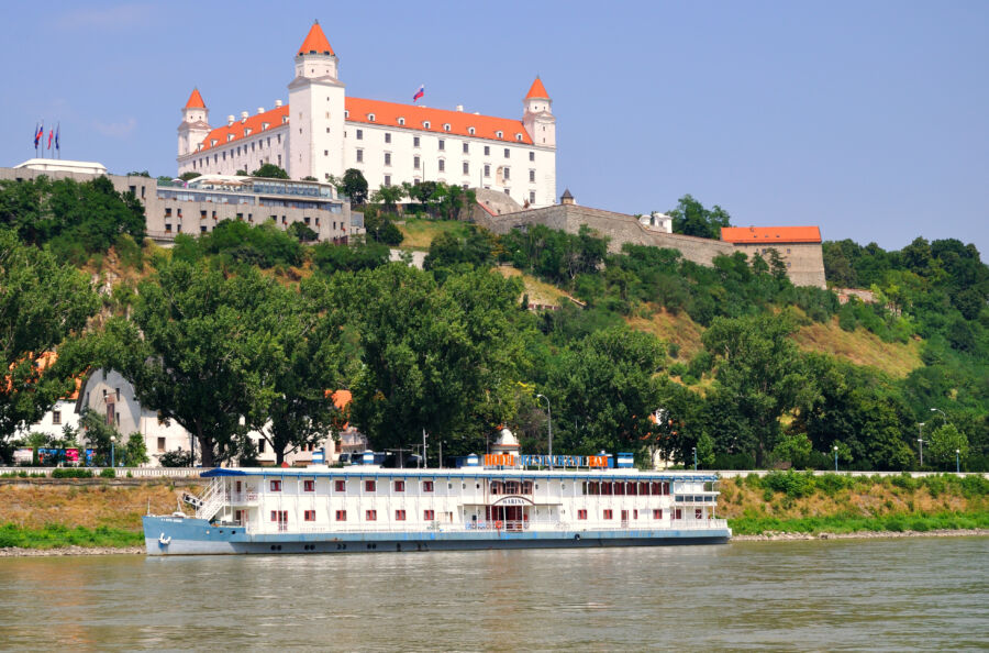 Bratislava Castle overlooks the Danube River, with a river cruise boat passing by