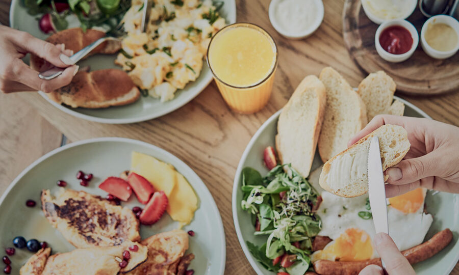 Vibrant breakfast spread with eggs, rolls, salad, fruit, orange juice, and sauces on wooden table.