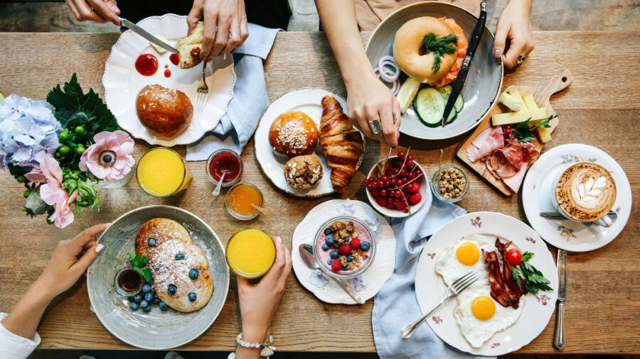 Vibrant breakfast spread with pancakes, eggs, fruits, pastries, and communal dining atmosphere.