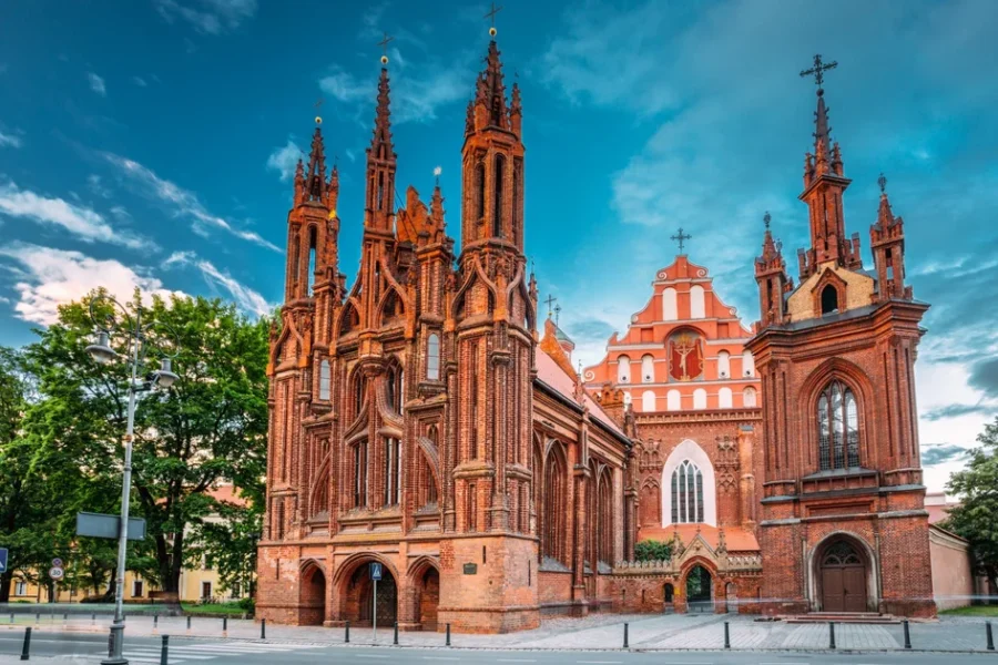 Brick Gothic St. Anne’s Church with spires and red brick facade under blue sky.