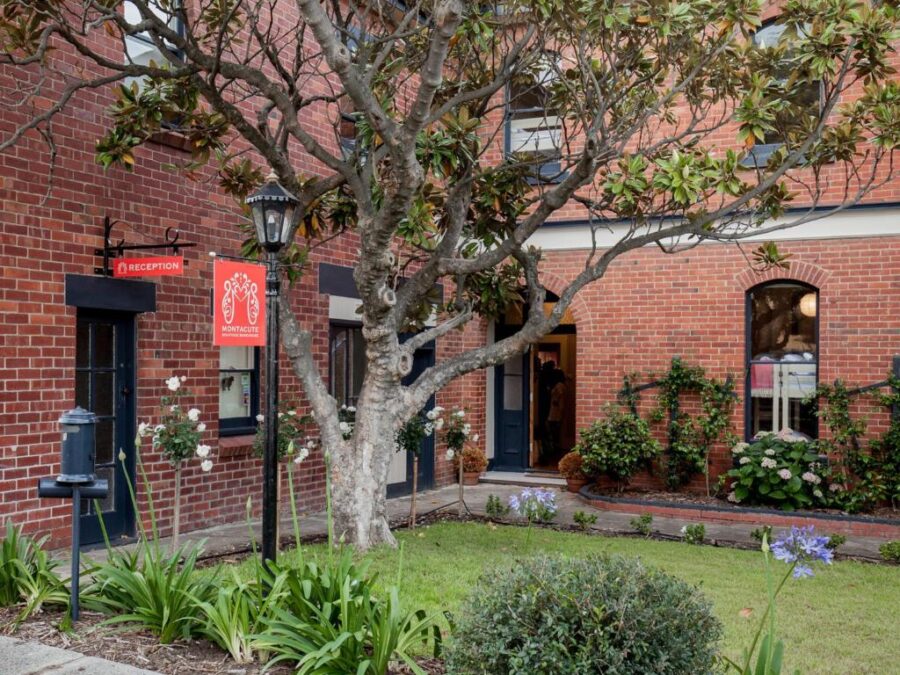Montacute Boutique Bunkhouse brick hotel reception with garden courtyard, tree, flowers, and arched windows.
