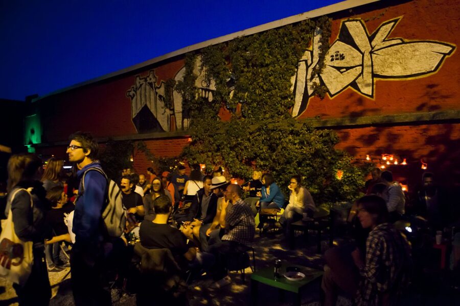 Evening outdoor courtyard gathering by brick wall with graffiti and ivy.