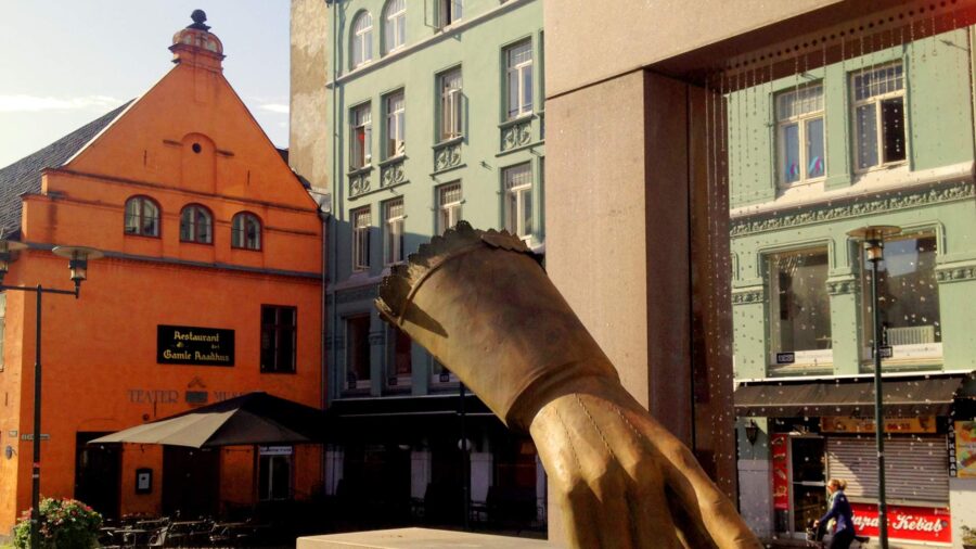 Bronze hand sculpture with water curtain in Kvadraturen city square with historic buildings.