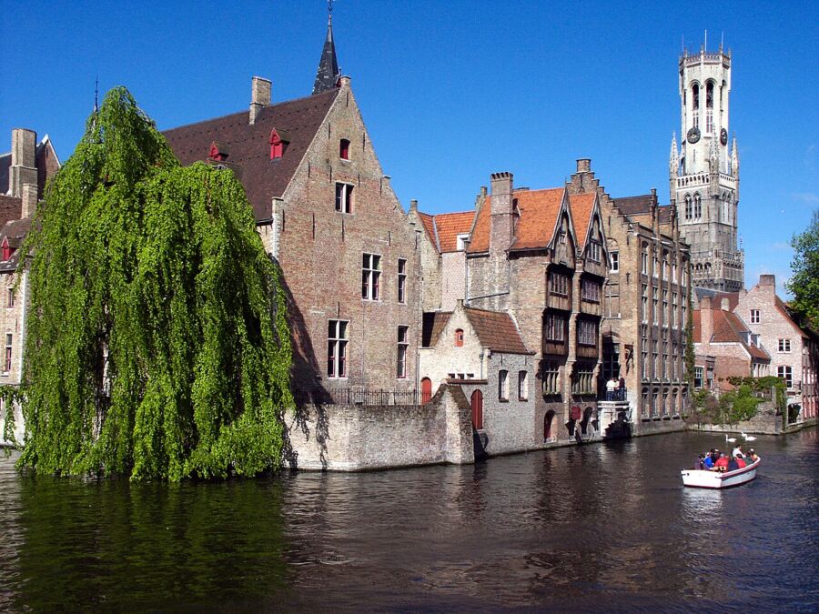 Scenic view of a boat navigating a canal in Bruges, Belgium, surrounded by charming architecture and reflections on the water.