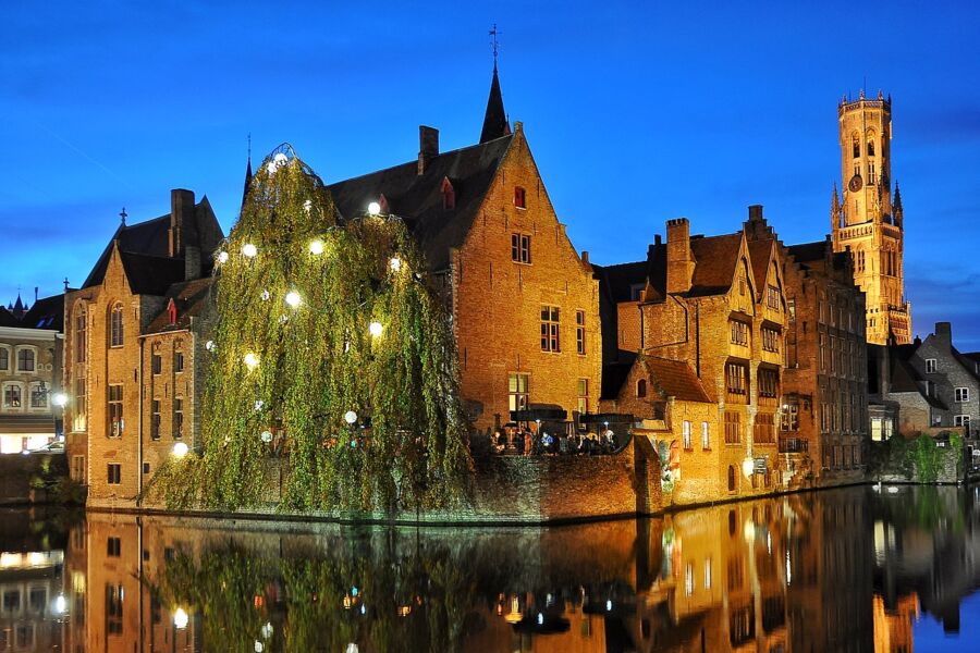 Night view of Bruges, Belgium, showcasing illuminated historic buildings and serene canals under a starry sky.