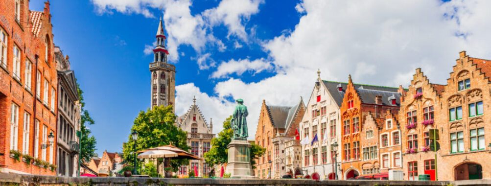 Panoramic view of Bruges, Belgium, showcasing medieval architecture and iconic towers under a sunny sky.