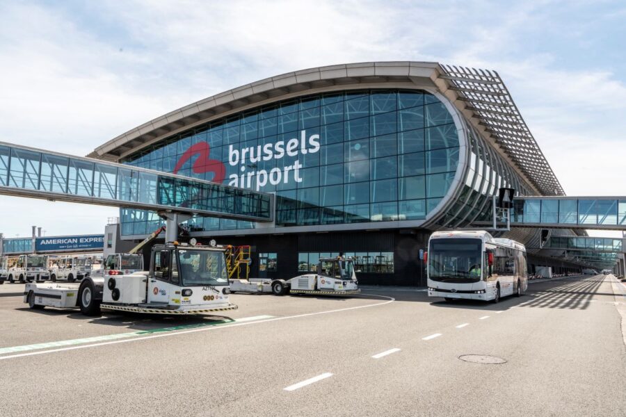Brussels Airport glass terminal and skybridge with ground service vehicles on apron.