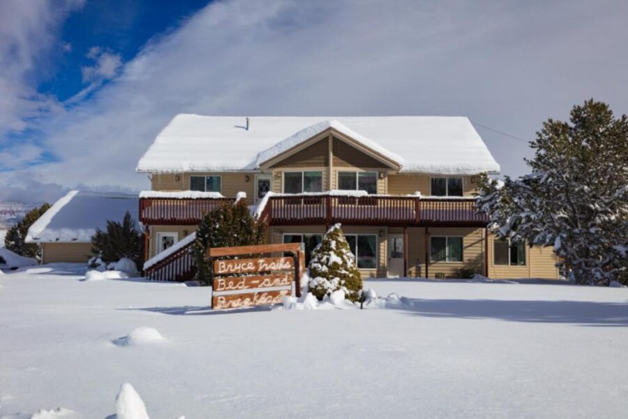 Snow blankets the ground around a large house, featuring a sign that says "Bryce Trails Bed and Breakfast."
