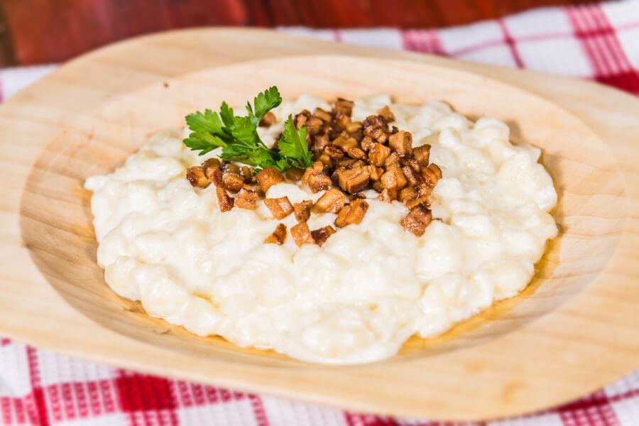Plate of bryndzové halušky, featuring potato dumplings topped with sheep cheese and crispy bacon