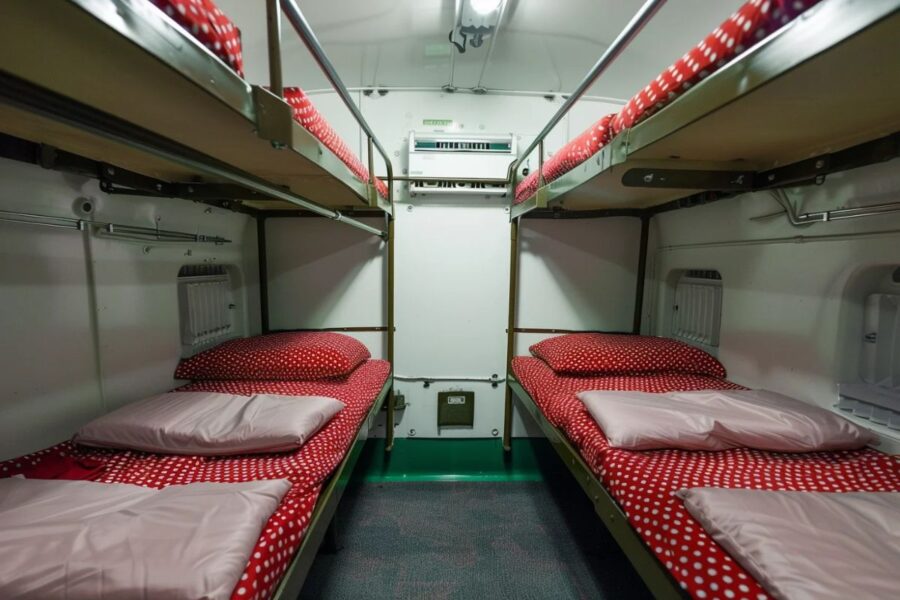 Compact bunk bed cabin with red polka dot mattresses, white walls, and bright lighting.