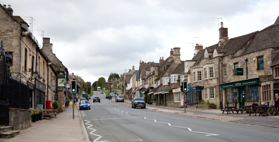 High Street in Burford, West Oxfordshire, featuring historic buildings and quaint shops under a clear blue sky.