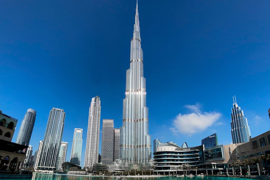 Dubais Burj Khalifa skyline, reflecting in water, under a clear blue sky.