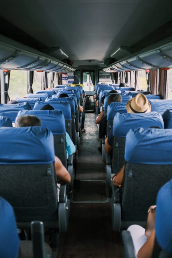 Interior of a bus with rows of blue seats and a few passengers, similar to a Nassau jitney.