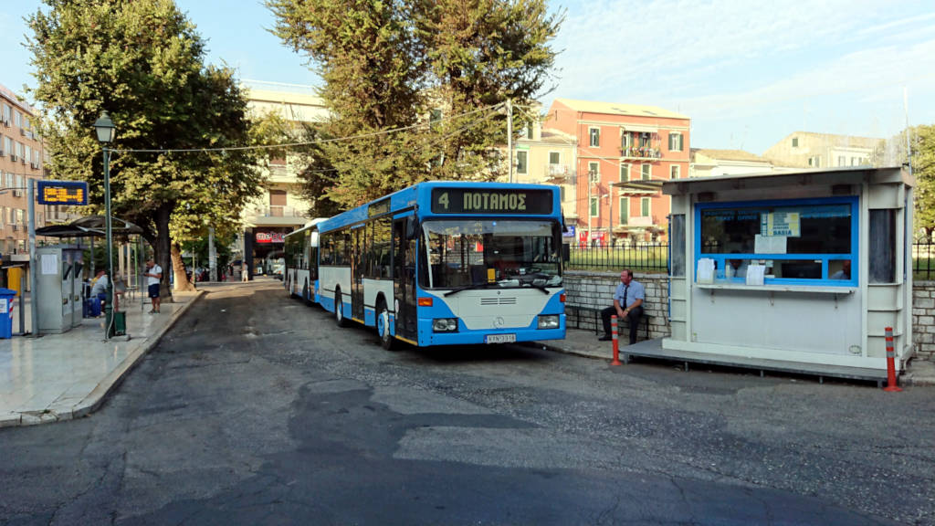City bus stop in Greece with route 4, kiosk, trees, and urban buildings.