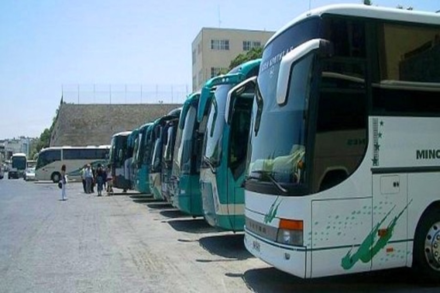 Teal and white buses parked in a sunny transit hub, people boarding, blue sky above.