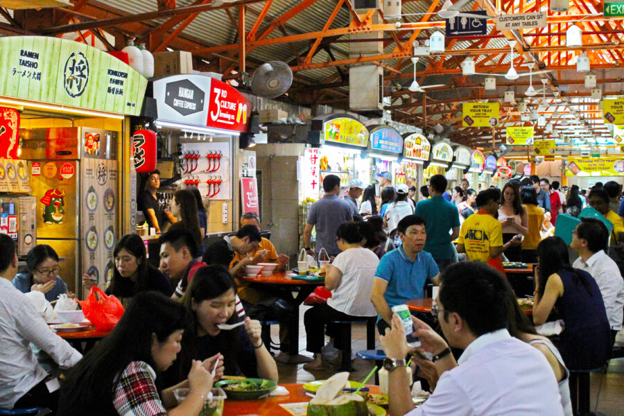 Busy food court with colorful stalls, diverse crowd, vibrant atmosphere, and various cuisines.