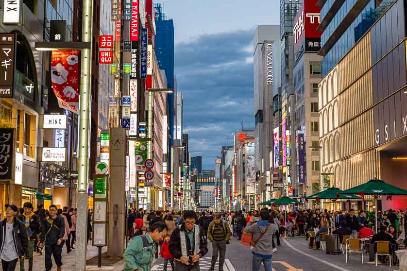 Ginza urban scene with vibrant shops, diverse crowd, and twilight skyline in Tokyo.