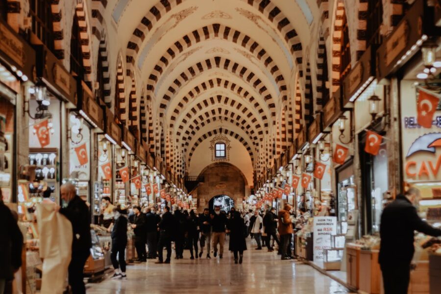 Bustling Turkish market with vaulted striped ceiling, vibrant stalls, and diverse shoppers.