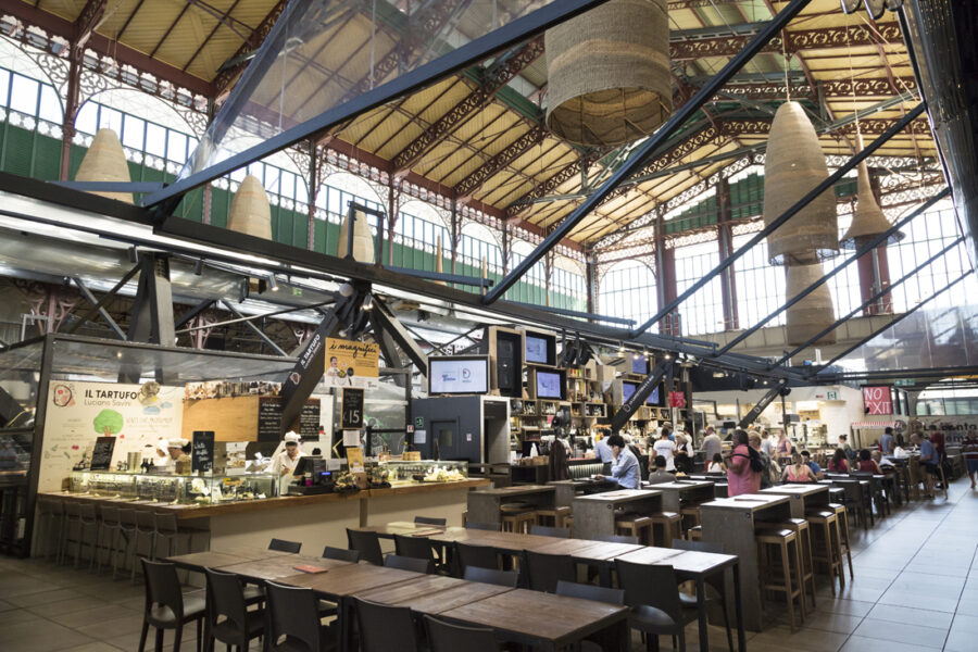 Vibrant market hall with diverse food stalls, lively dining, and unique architectural design.