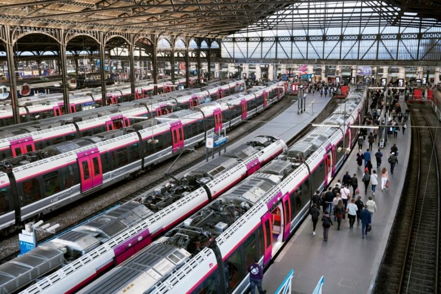 Modern railway station with sleek white and pink trains, bustling travelers, and arched steel architecture.