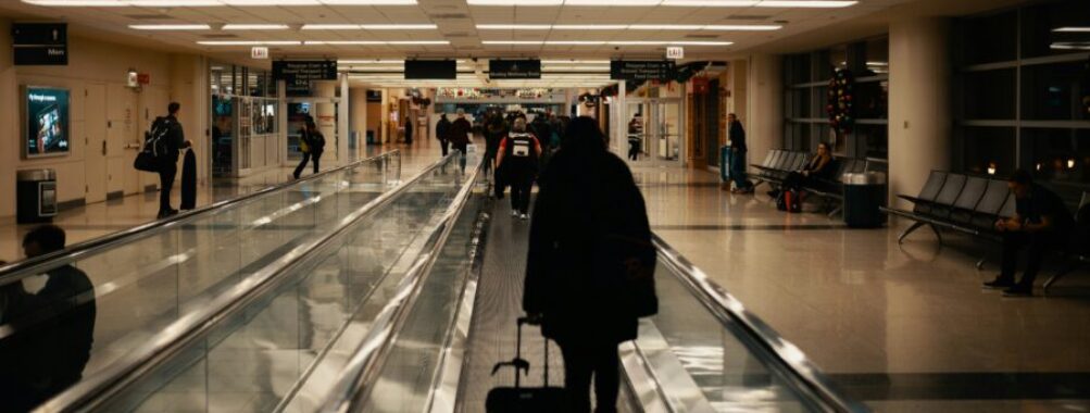 Bustling airport terminal with travelers, bright lights, and high ceilings at night.