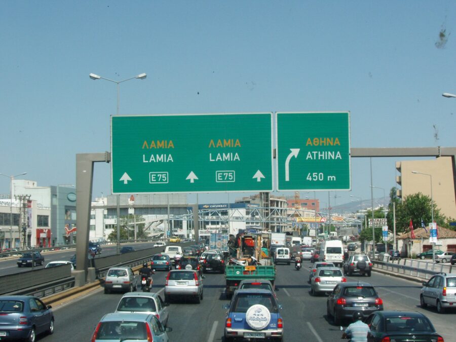 Busy Greek highway E75, road signs for Lamia and Athens, cars, clear blue sky.