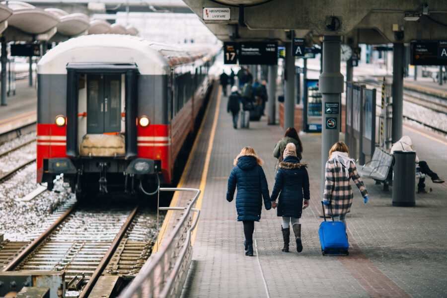 Travelers with a bright blue suitcase walk along a busy train station platform on a chilly day.