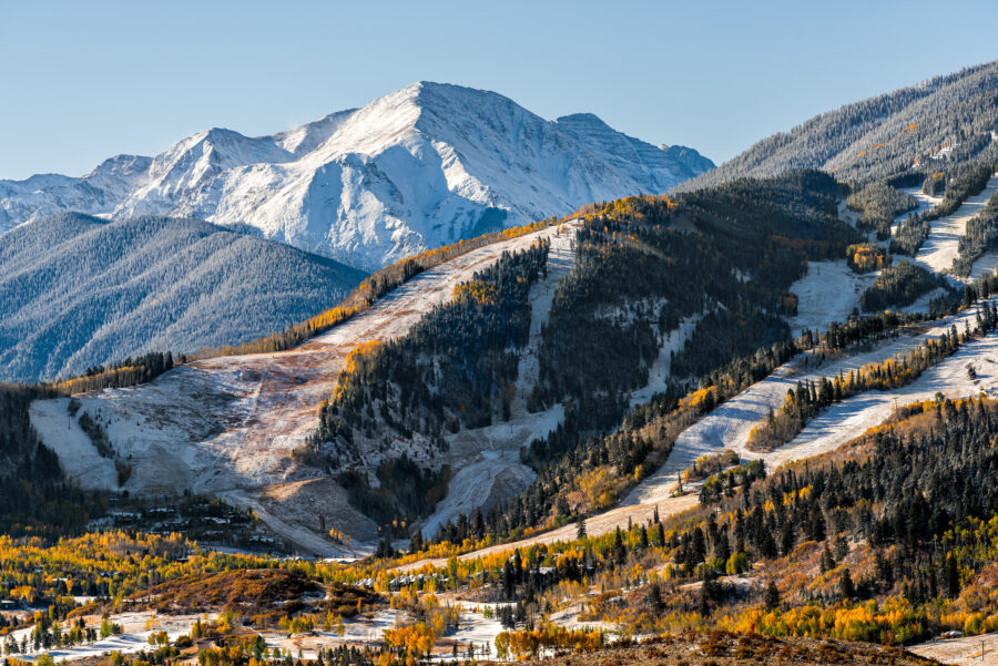 Scenic peak of Aspen's ski slope with snow-covered hills and vibrant autumn foliage on a sunny day in the Rocky Mountains
