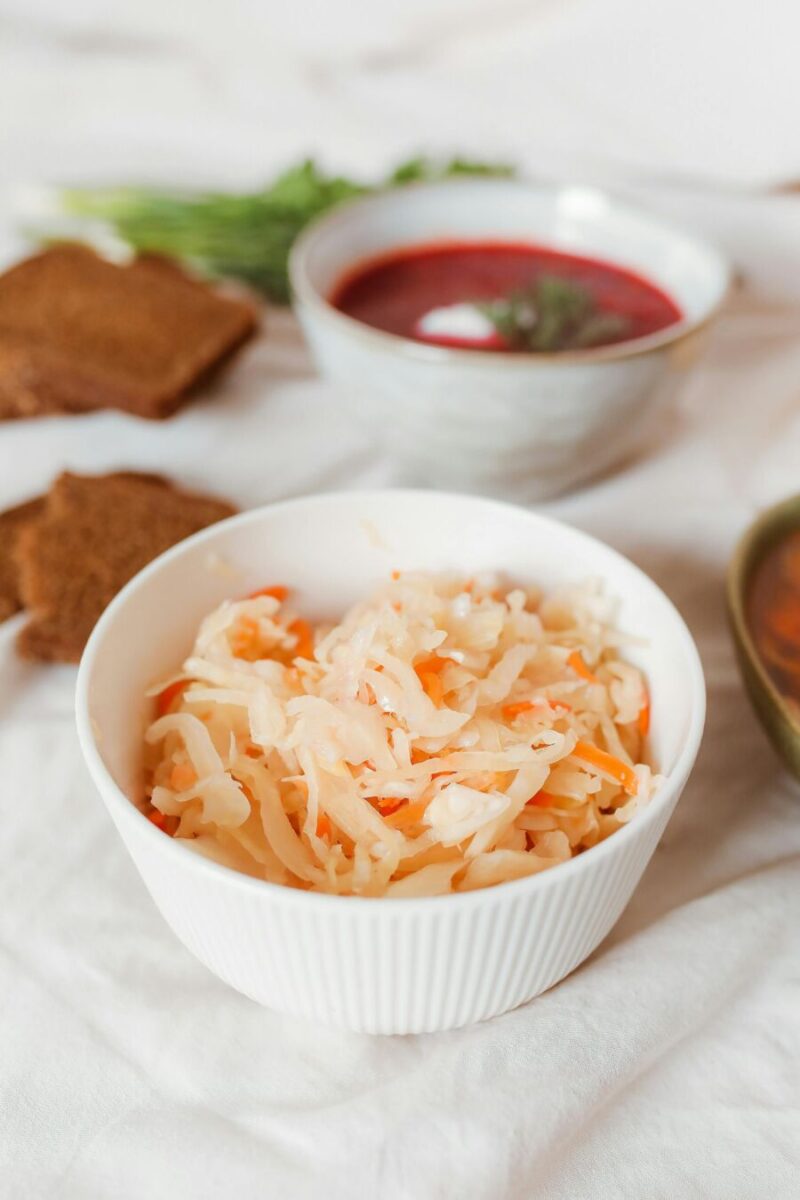 Traditional cozy meal with sauerkraut, beet soup, fresh herbs, and rye bread on rustic fabric.