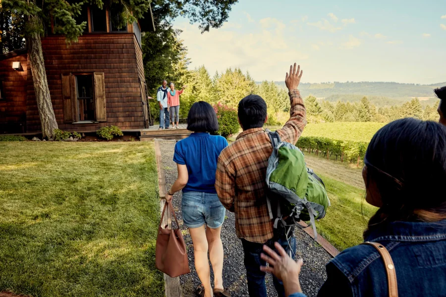 Friends departing a rustic cabin amidst greenery, capturing a joyful farewell moment.