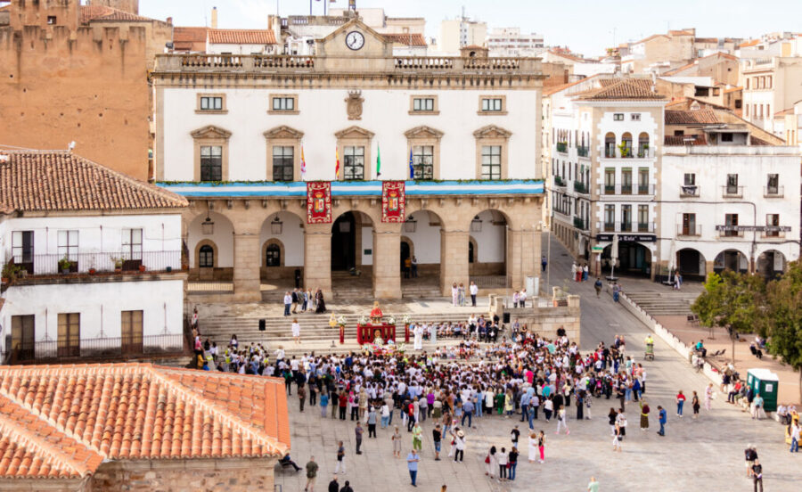 Community gathering at historic building in Cáceres, Spain, with diverse crowd and festive atmosphere.