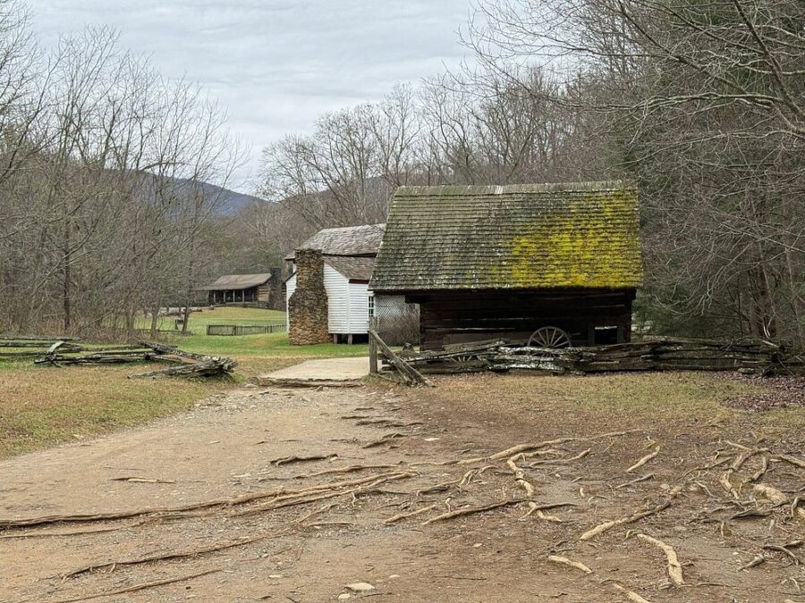 Rustic cabin sits at the end of a dirt road, enclosed by a simple wooden fence amidst a tranquil landscape.