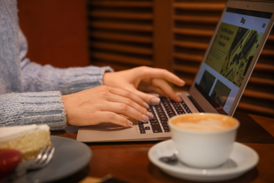 Young woman using a laptop in a cafe, with a cup of coffee beside her, focused on her work.