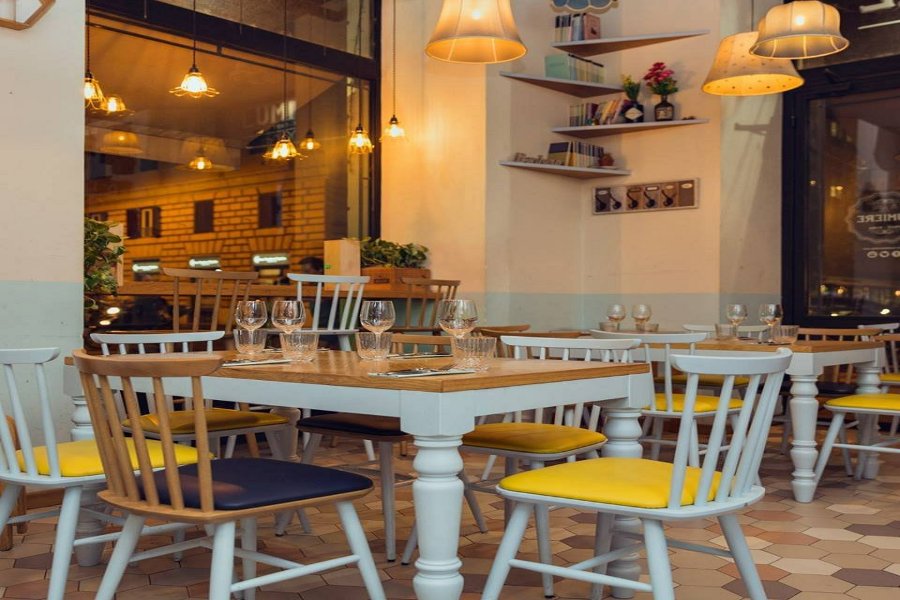 Cozy bistro interior with warm pendant lights, wooden tables, blue chairs, and evening street view.