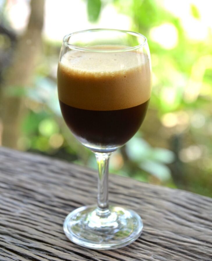 Glass of Caffè Shakerato on a table, showcasing its rich coffee color and frothy top.